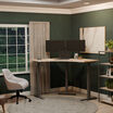 A minimalist home office featuring a light wood L-shaped standing desk with dual monitors, a laptop, and a cozy upholstered chair, set against dark green walls and a large window with garden views.